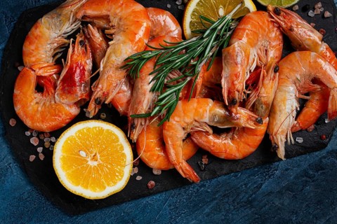 Freshly frozen shrimp, with lemon and rosemary, on black slate, close-up, top view, no people