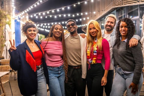 Portrait of multi-ethnic young friends standing smiling at camera in a bar terrace at night