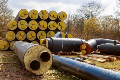 Stacked district heating pipes with yellow ends lie piled up in a meadow