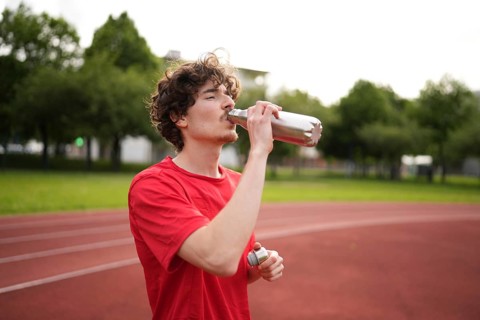 Thirsty caucasian young amle athlete drinking water in a reusable bottle after training in a