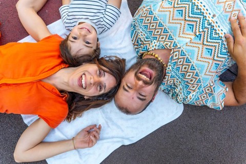 A family of three, a man, a mother and a son, are laying on a blanket on the ground. The man is