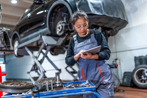 Young woman mechanic using a digital tablet, inspecting car parts and components in a professional