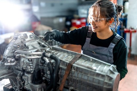 Asian woman mechanic working diligently on a vehicle gearbox in a professional garage, showcasing