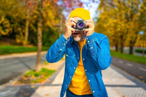 Surprised modern mature man tourist photographing in the city street during fall
