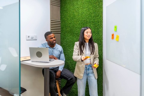Two managers are discussing a project using sticky notes on a whiteboard in a modern coworking