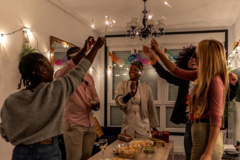 Multi-ethnic happy friends raising burning sparkler celebrating party at night at home