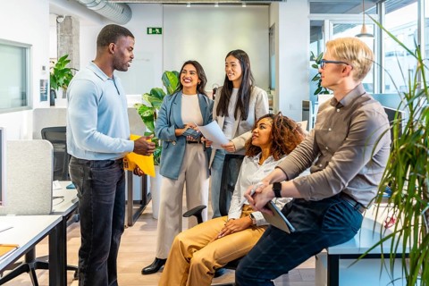 Five coworkers are discussing a project, sharing ideas and documents, in a modern coworking office