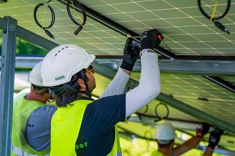 Workers install solar panels wearing safety helmets and high-visibility waistcoats, construction of