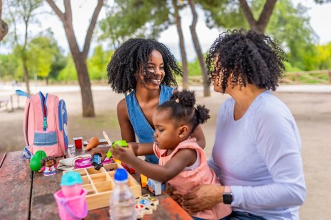Happy african girl playing with toys sitting in a park with her mother and grandmother