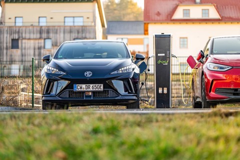 A black electric car being charged next to a charging station in a rural area, Deer E- Carsharing