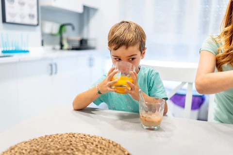 School boy drinking orange juice at home with his mother at the side before going to school