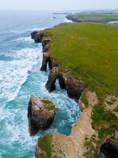 Impressive view of steep cliffs with unique rock formations and a lush green landscape, aerial