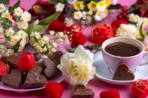 Coffee mug with chocolate and flower arrangement on a pink background, Valentine's Day