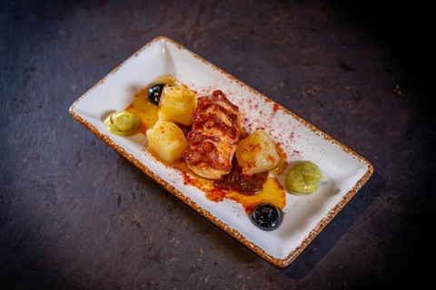 Octopus tentacle with potatoes on a black background, on a white plate