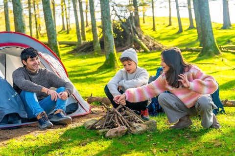 Brother and dad preparing bonfire next to camping tent in an alpine forest