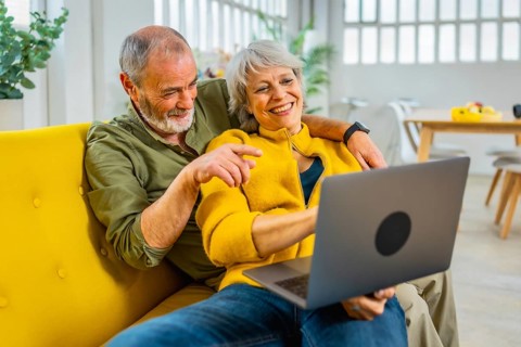 Mature woman lying on her husband sharing laptop on sofa in a cozy modern apartment