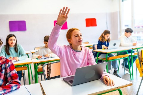 Smart student raising hand to answer teacher's question in modern classroom with laptops and