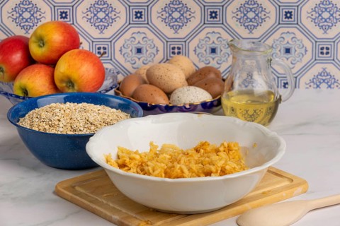 Grated apple in a bowl in front of oat flakes, eggs and honey