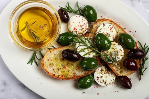 A plate with a snack, ciabatta bread with cheese and olives, olive oil, spices and herbs, top view,
