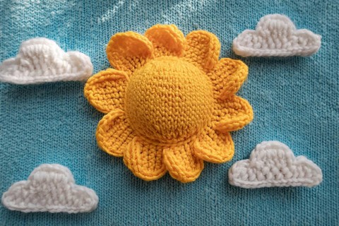 Crocheted yellow sun and white clouds on a light blue knitted background, AI generated, AI