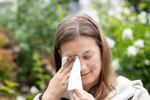 Young woman suffers from hay fever and uses a paper handkerchief outdoors, Freiburg,