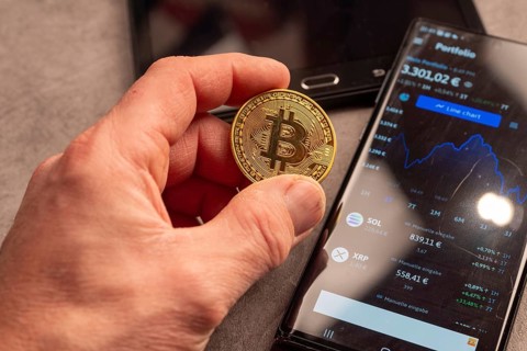 A hand shows a Bitcoin coin next to a smartphone with portfolio data