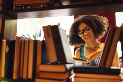 Happy African American female student studing in university library and looking for the book,