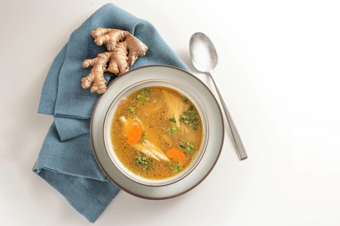 Healthy soup from chicken meat, vegetables and ginger in a bowl on a blue napkin and a gay white
