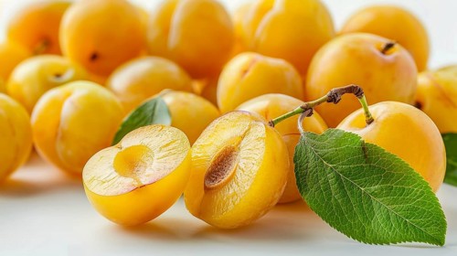Fresh yellow plums (Prunus domestica) with leaves on a white background, emphasizing their natural