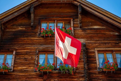 Beautiful Old Town with a Wood House with Flower and Swiss Flag in a Sunny Summer Day in Andermatt,