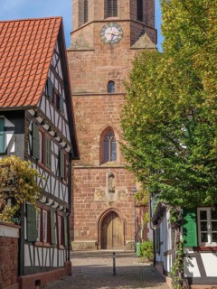 View of church with clock and half-timbered houses in a small cobbled village street, Kandel,