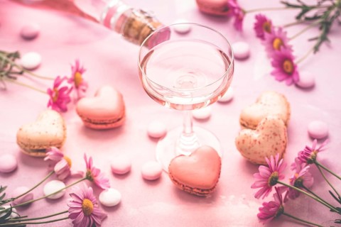 Happy Mothers Day - sweet macarons in heart shape and glass of rose sparkling wine with flowers in