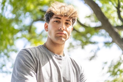 Confident young blonde man portrait, summer trees background.
