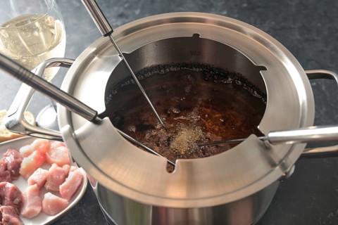 View into a fondue pot with boiling hot oil, long forks, pieces of meat and wine, festive dinner