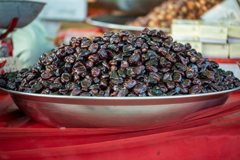 A large pile of shiny dark dates displayed on a metal plate at a market stall