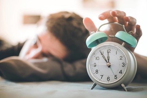 White alarm clock in the morning. Young man wakes up