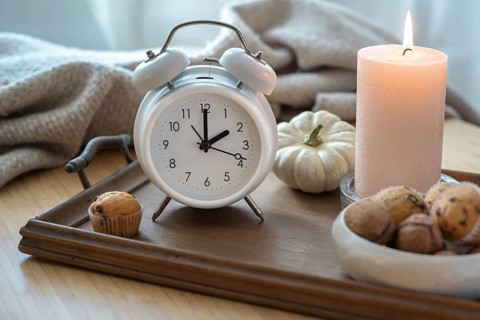 White vintage alarm clock, candle, autumn decoration and sweets on a nightstand with a natural