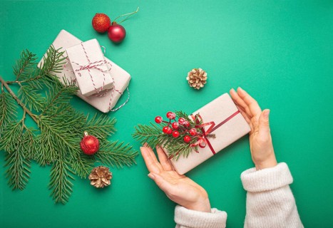 Christmas or New Year celebration green paper festive background with female hands holding wrapped