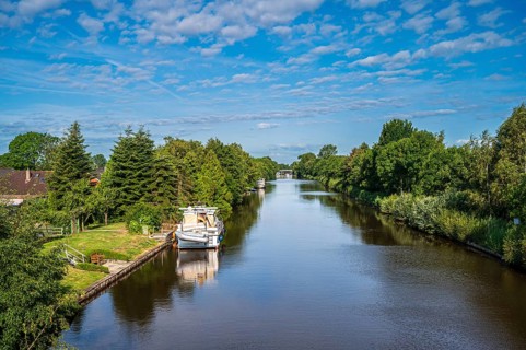 A canal surrounded by lush greenery under a slightly cloudy sky with a boat, Ems-Seitenkanal,