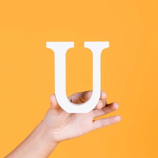 Female hand holding white uppercase alphabet u yellow surface