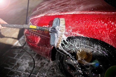 Washing a soapy red car focusing on the side and tire with a brush