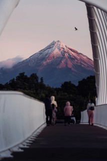 People on a bridge admiring a snow-capped mountain at sunset with a bird in the sky, Mount