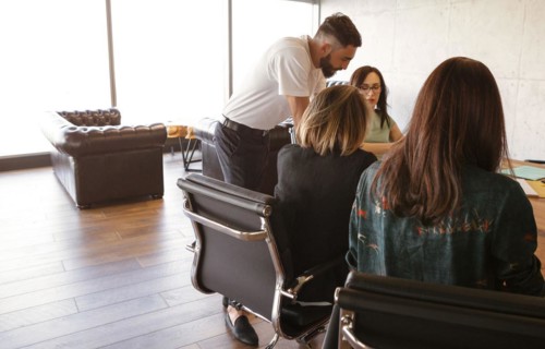 Smiling diverse colleagues gather in boardroom to discuss financial statistics together, happy
