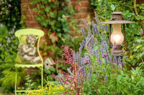 A garden with a statue of an angel on a green chair, surrounded by flowering plants and a burning