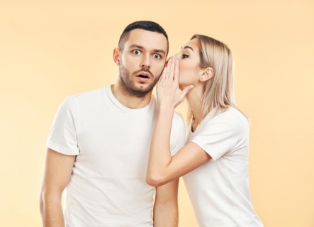 Young woman whispering secrets to man over beige background. Gossiping, couple relationship concept