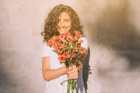 Young woman standing against wall holding (alstroemeria) red flower bouquet hands
