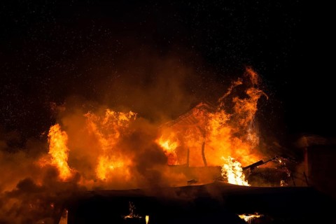 Arson or nature disaster, burning fire flame on wooden house roof