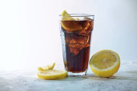 Fresh cola with ice cubes and lemon slices in a drinking glass against a light blue gray