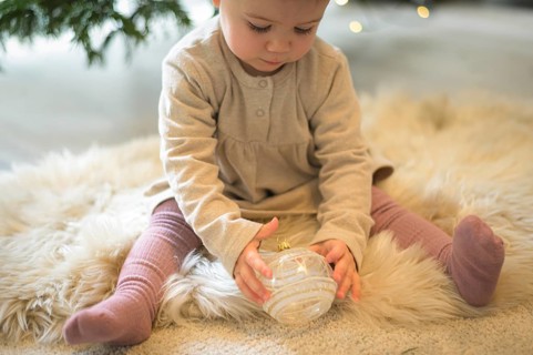 Toddler sitting on a rug and looking at a Christmas tree bauble in a cosy setting