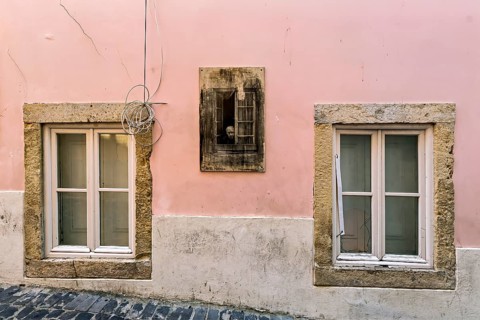 Facade of an old building with pastel pink walls and stone-framed windows with closed wooden
